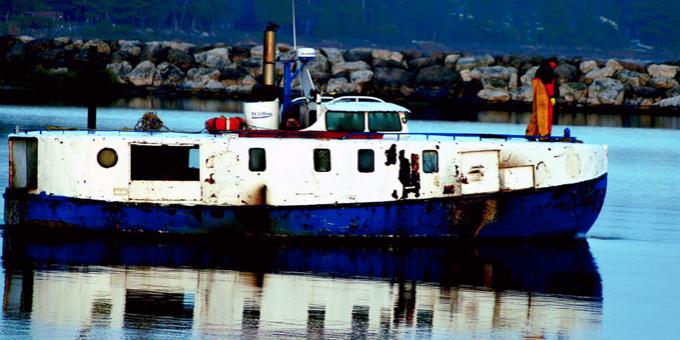 A commercial fisher in orange waders at the bow of a boat.