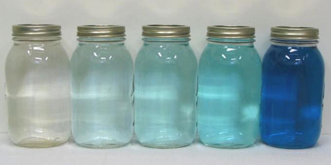 A series of jars with a spectrum of tinted blue liquid from clear to dark.