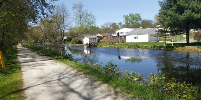 A gravel towpath runs parallel to the Ohio-Erie Canal with houses along its banks.
