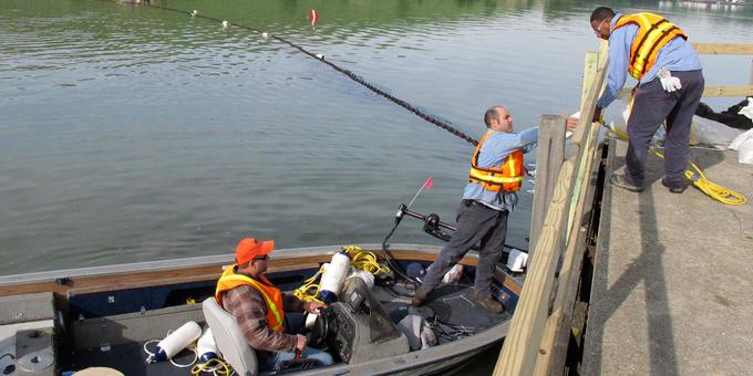 A person hands sampling equipment to another person on a boat.