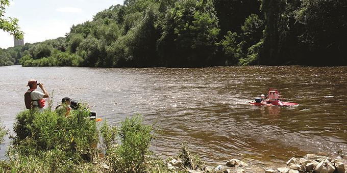 Water sampling equipment floats in a river while biologists view it from the shore.