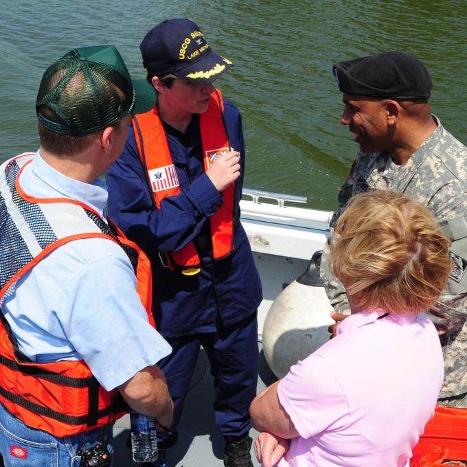A group of people standing at the back of a boat talk with one another.