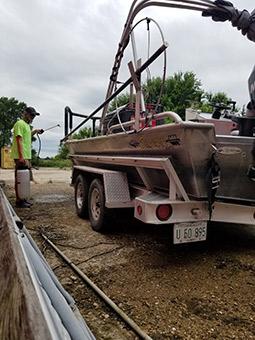 A person wearing a protective cloth face masks holds a chemical sprayer in his hands pointing the nozzle at a boat.