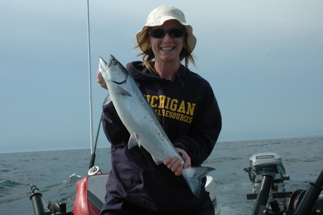 A recreational fisher out on a boat holding a fish for a photo.