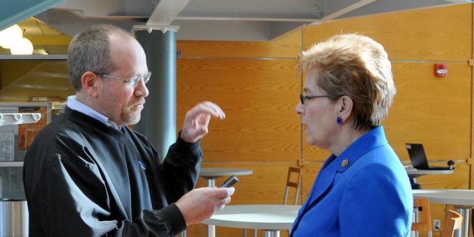 A woman in a blue blazer speaks with a man holding a voice recorder.