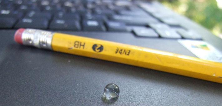 A tiny round transparent sphere sits on a laptop near a pencil.
