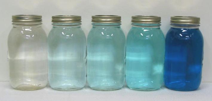 A series of jars with a spectrum of tinted blue liquid from clear to dark.