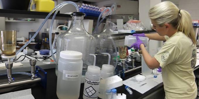 A biologist among laboratory equipment pours liquid into a small container.