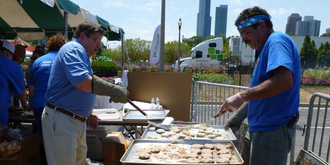 Two men stand near a grill with spatulas.