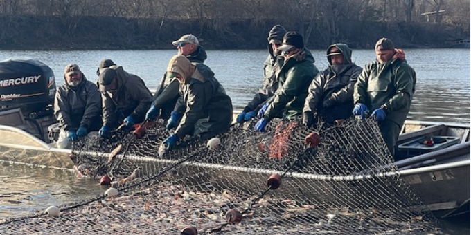 A group of people standing in a boat pulling in a fishing net.