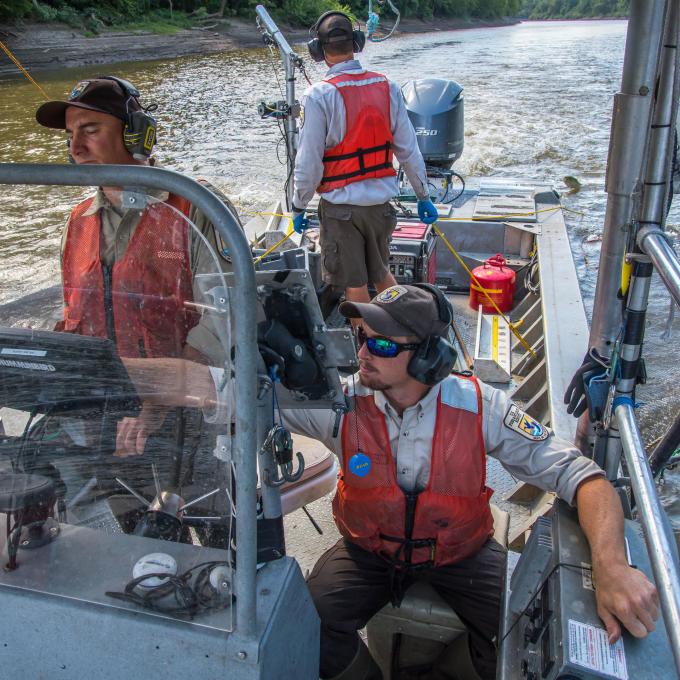 Three biologists in a flatbottom boat. One is driving as another points to a screen in front of them.
